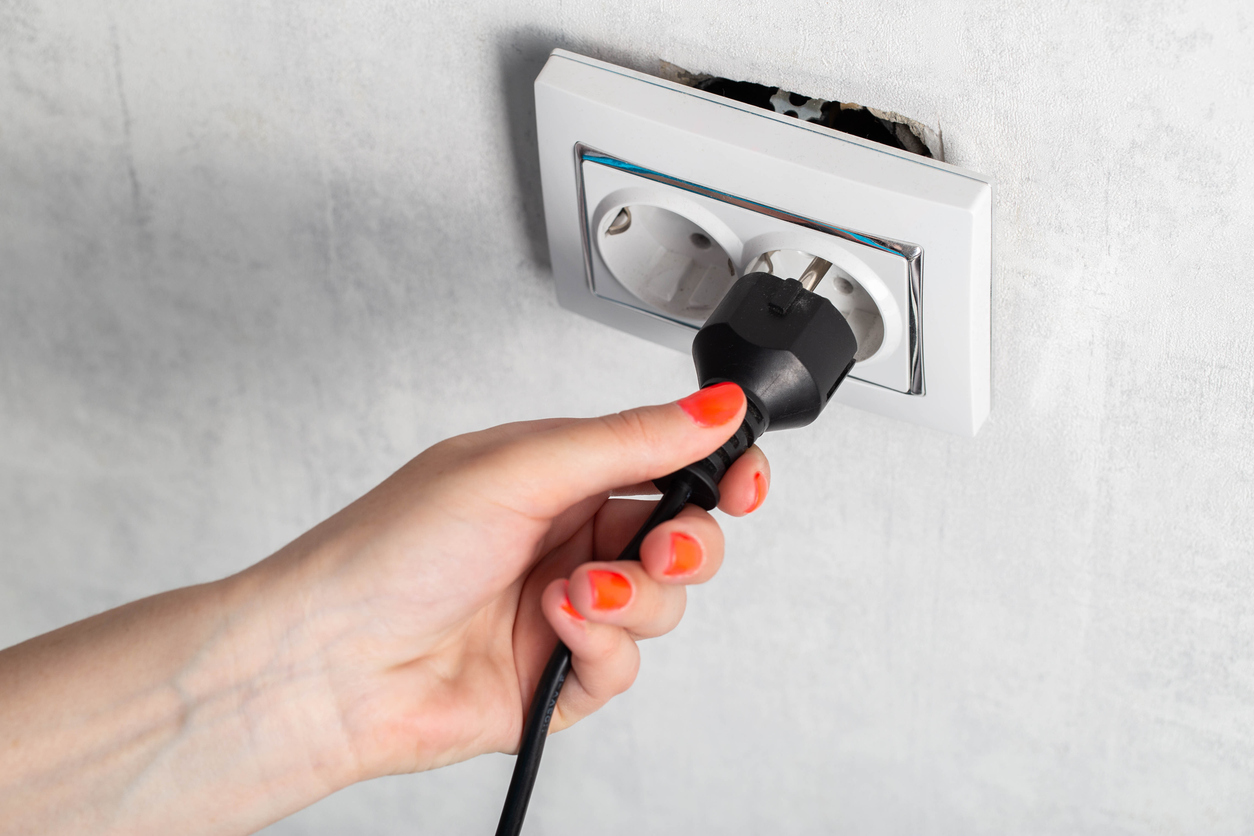 Hand plugging into an outlet with a loose cover, a common home electrical troubleshooting issue.