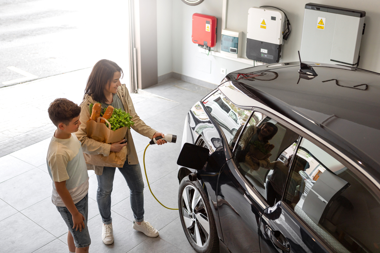 A parent with groceries plugs an EV into a garage wall charger, for cheaper, more convenient home EV charging.