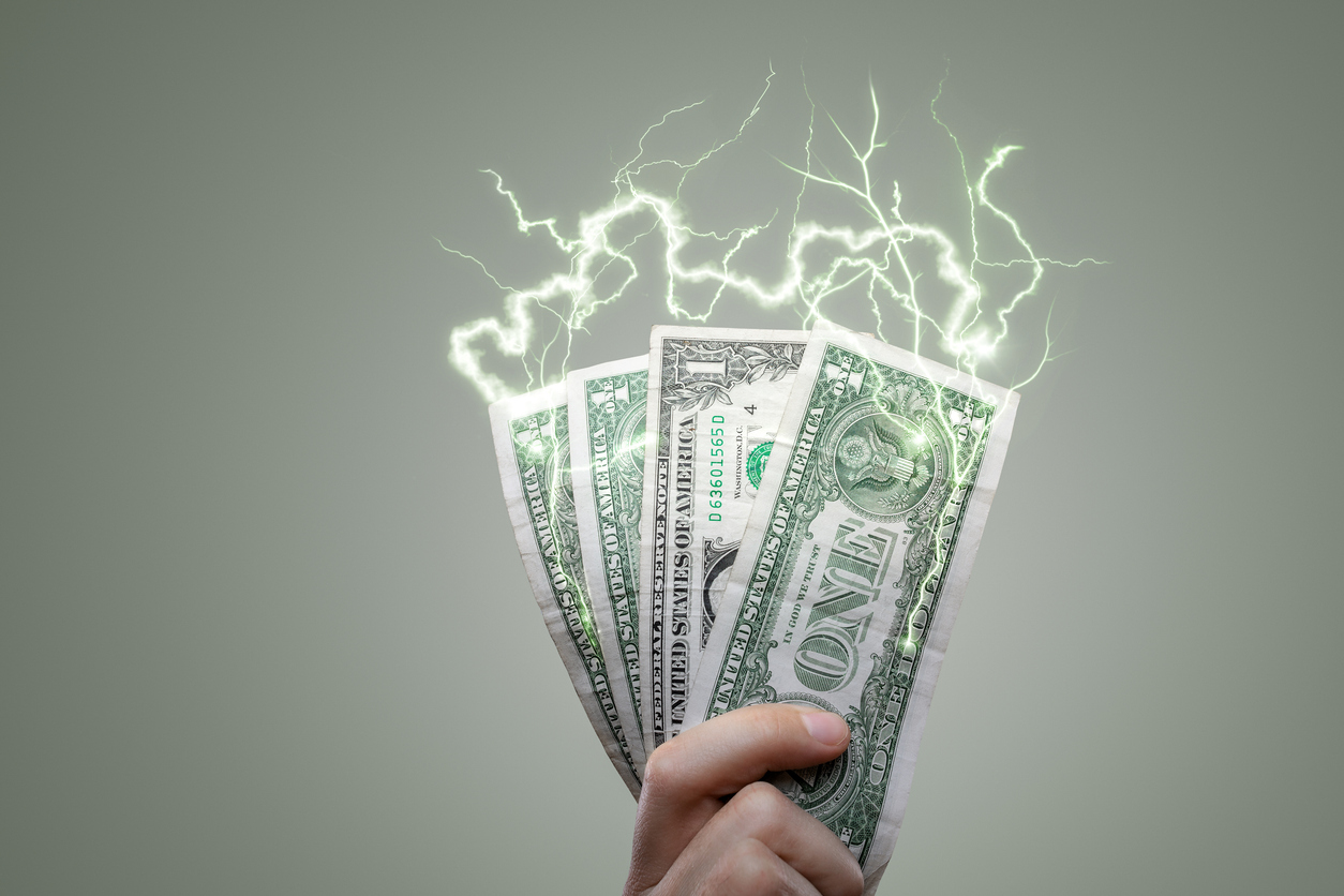 Hand holding dollar bills with electric lightning bolts, symbolizing how home appliances drain electricity and money.