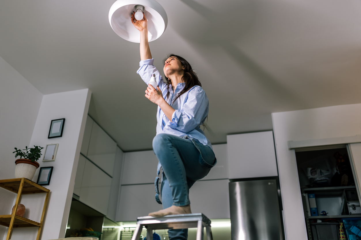 Woman swapping out a ceiling light bulb as part of a home energy-saving upgrade.