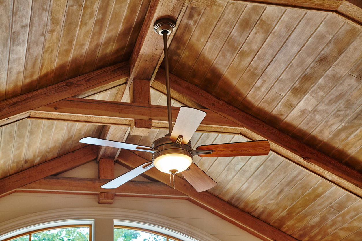 Ceiling fan mounted on a downrod below a vaulted wooden ceiling with exposed beams.