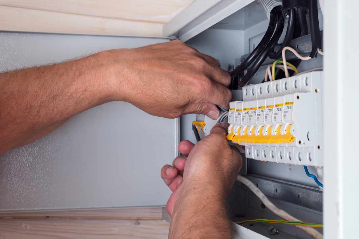 Electrician connecting cables in an open residential electrical panel with rows of circuit breakers inside.